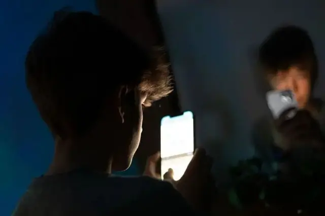 تصویر پسر نوجوانی از پشت سر در حال نگاه کردن به موبایلش