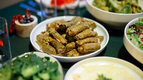 Plate of neatly rolled stuffed grape leaves served alongside salads and other dishes on a dining table (Credit: Getty Images)