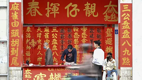 People stand behind a red stall in China while others move past on the street (Credit: Getty Images)