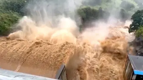 A huge volume of brown water rushes through a dam